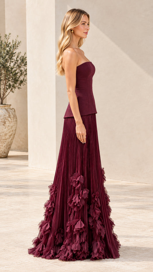 Burgundy strapless pleated evening gown with floral details three-quarter side view