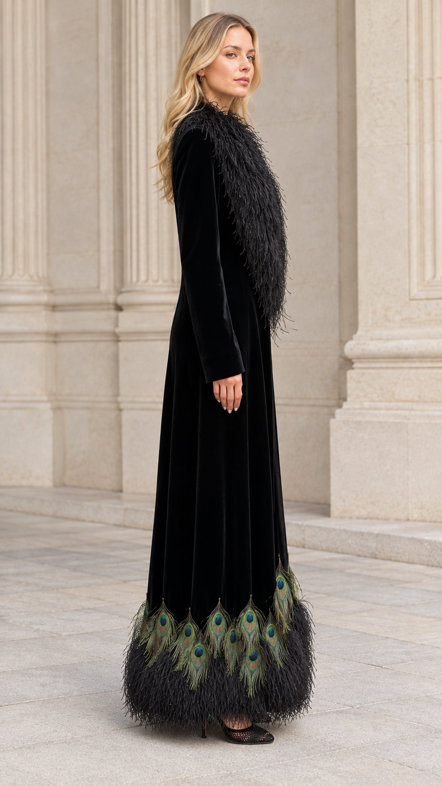 Side angle of model wearing black velvet floor length coat with peacock detail