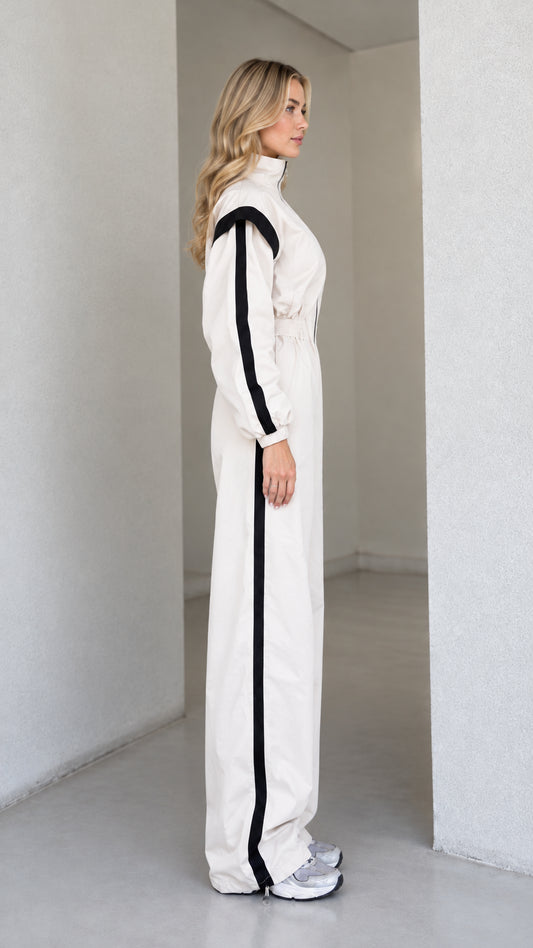 Side profile view of women's cream zip-front track jumpsuit