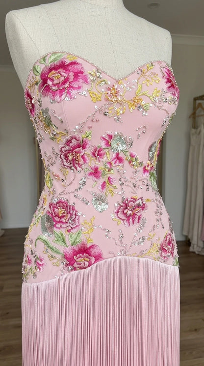 Close-up detail of mannequin displaying blush pink floral sequin embroidery and fringe