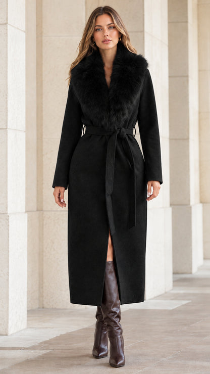 Front view of woman wearing black belted maxi coat with matching black faux fur collar