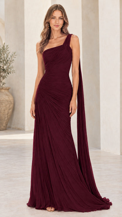 Front view of model wearing burgundy one-shoulder pleated evening gown with shoulder cape